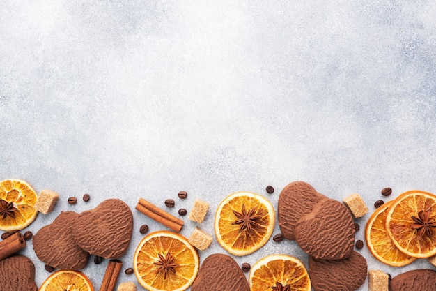 Chocolate heart cookies, oranges cinnamon and spicy spices on a gray table, top view, copy space.