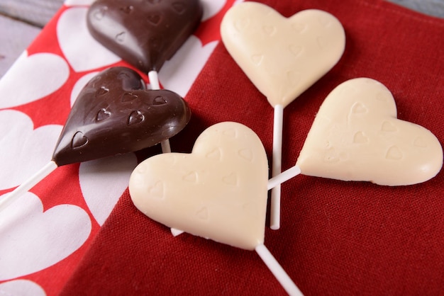Шоколадные конфеты в форме сердца на палочках на красной салфетке, крупным планом
