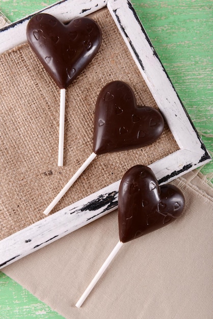 Foto caramelle a forma di cuore di cioccolato su bastoncini su tela di sacco, primo piano