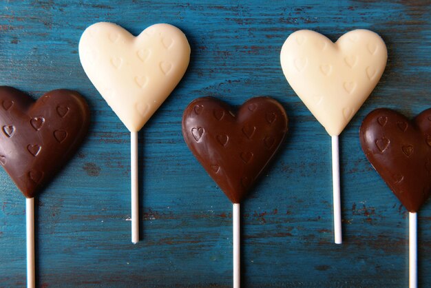 Chocolate heart shaped candies on sticks on wooden background