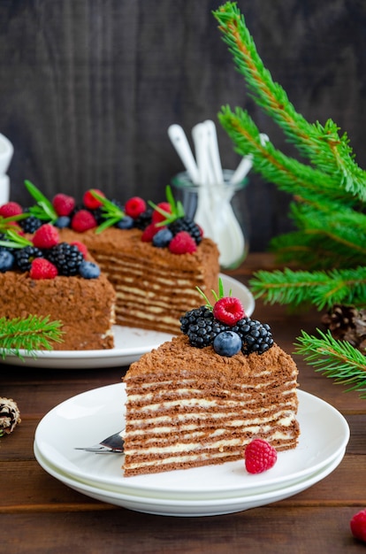 Torta al cioccolato e miele con panna e frutti di bosco freschi in cima su un piatto bianco su un tavolo di legno.