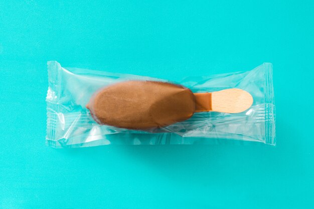 Chocolate ice cream popsicle wrapped in plastic bag isolated on blue