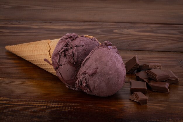 Chocolate ice cream scoops in waffle cones and chocolate pieces on wooden background.