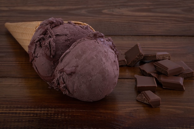 Chocolate ice cream scoops in waffle cones and chocolate pieces on wooden background.