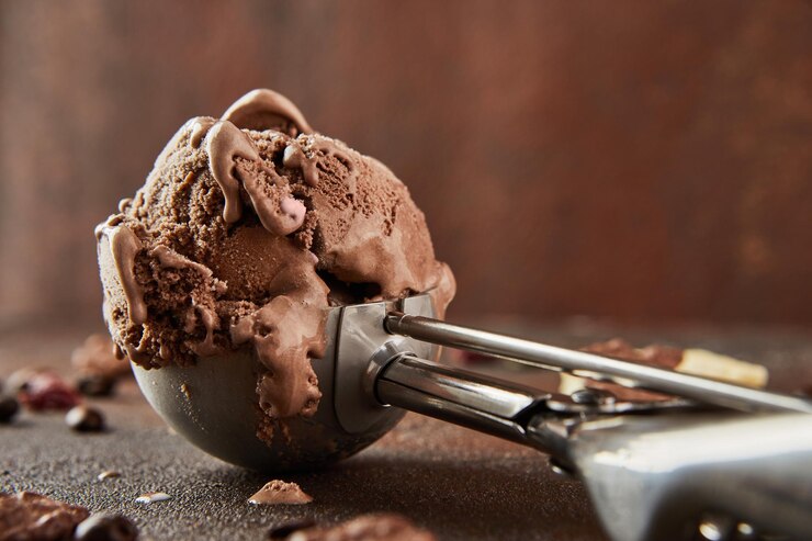 Photo chocolate ice cream in special metal spoon for rolling balls on brown concrete background