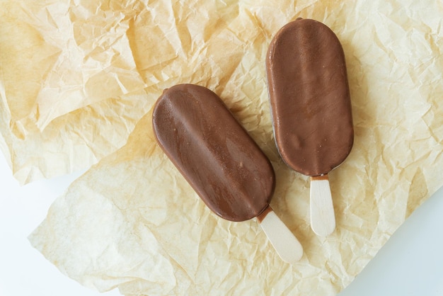 Chocolate ice cream on a stick lies on parchment covered with chocolate warm cold delicious