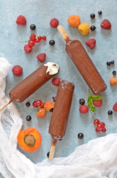 Gelato al cioccolato su bastoncini con frutti su una superficie blu