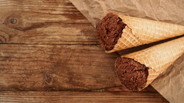 Chocolate ice cream in a waffle cone on craft paper on a wooden background