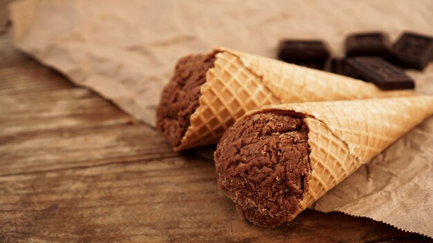 Chocolate ice cream in a waffle cone on craft paper on a wooden background