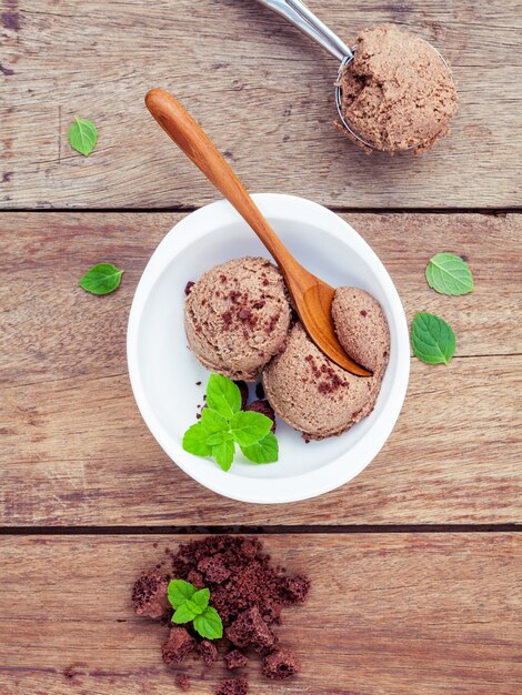 Chocolate ice cream in white bowl with fresh peppermint leaves  setup on wooden background .