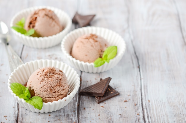 Chocolate ice cream in a white bowls on a wooden table.