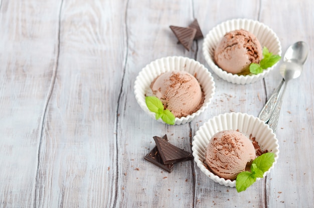 Chocolate ice cream in a white bowls on a wooden table.