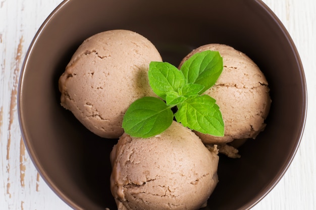 Chocolate ice cream with mint leaf in brown bowl, top view