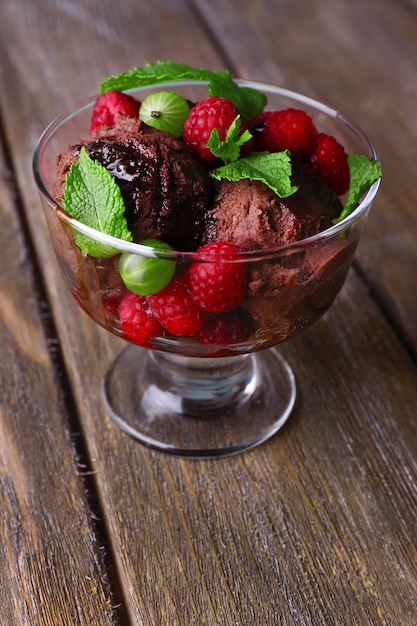 Chocolate ice cream with mint leaf and ripe berries in glass bowl on color wooden background