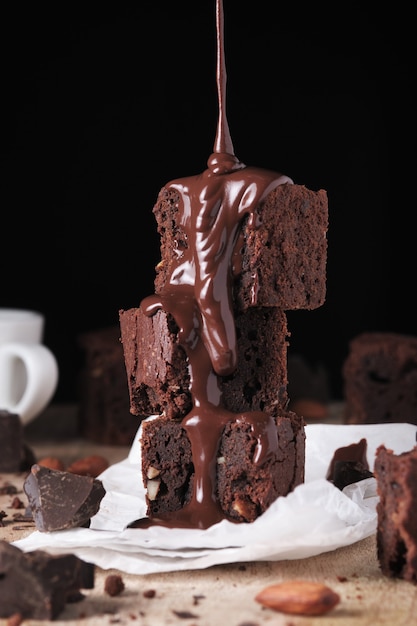 Chocolate is poured on brownie with nuts Sweet and tasty dessert closeup on a wooden table