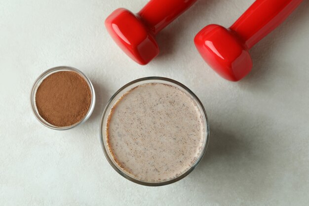 Chocolate milkshake, chocolate powder and dumbbells on white textured table