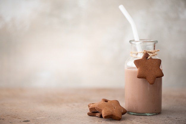 Chocolate milkshake in glass bottle with gingerbread crumbly cookies on table