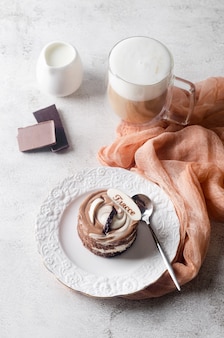 Mini torta al cioccolato in elegante piatto bianco e cappuccino con schiuma in tazza di vetro su sfondo grigio chiaro, vista dall'alto. delizioso dessert. regolazione del posto del tavolo della colazione.