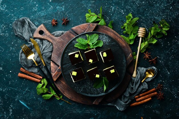 Шоколадный муссовый десерт Опера на черной тарелке с мятой Вид сверху Деревенский стиль