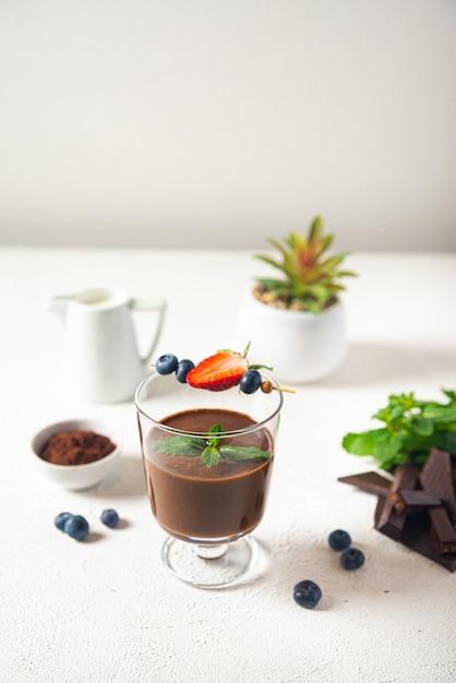 Chocolate mousse in a glass with berries and mint on a light background