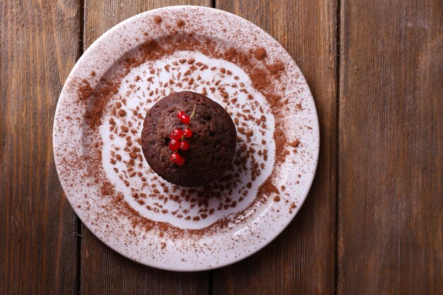 Chocolate muffin with red currant on plate on wooden background