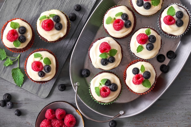 Muffin al cioccolato o cupcakes con panna montata e frutti di bosco in piatti di metallo