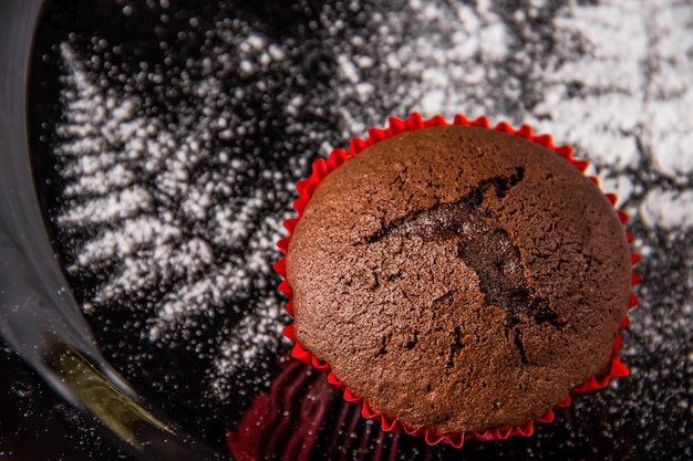 Chocolate muffins on a dark background with a twig decoration painted with icing sugar