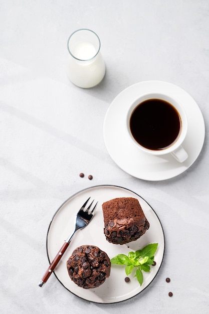 Chocolate muffins on a white plate with mint on a light background with cup of coffee and milk The concept of healthy homemade baked for breakfast