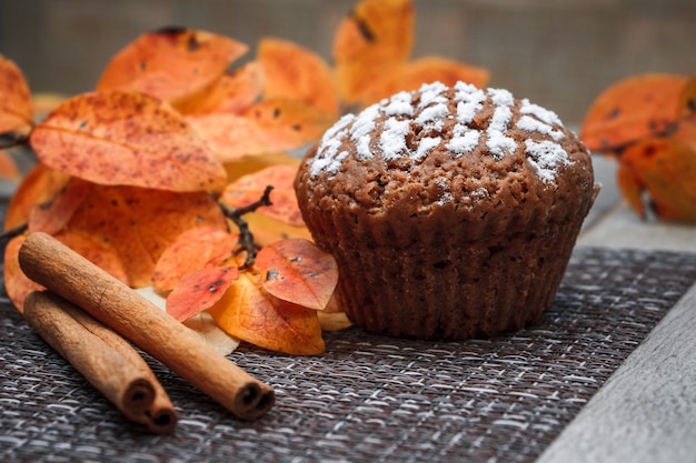 Muffin al cioccolato con ripieno di mele su uno sfondo di foglie autunnali e cannella