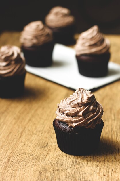 Chocolate muffins with cream on a wooden background