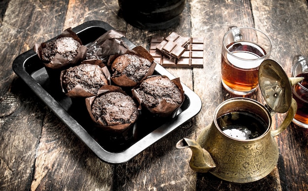 Chocolate muffins with fragrant tea on wooden table.