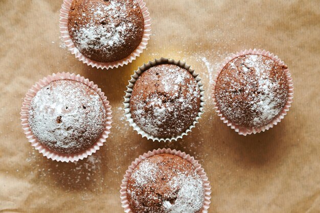 ベーキングペーパーに粉砂糖を入れたチョコレートマフィン。上面図、食品の背景、フラットレイ。