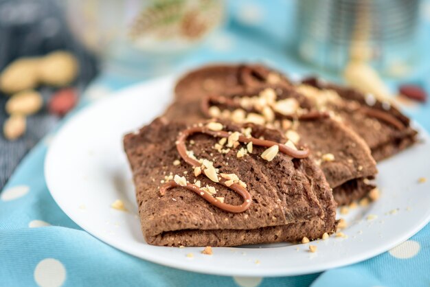 Chocolate oat pancakes with caramel and nuts on grey wooden table.