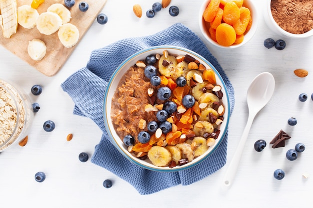 Chocolate oatmeal porridge with blueberry, nuts, banana, dried apricot for healthy breakfast. Top view