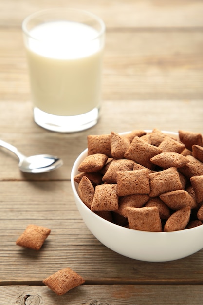 Chocolate pads corn flakes and milk in bowl on grey background. Vertical photo