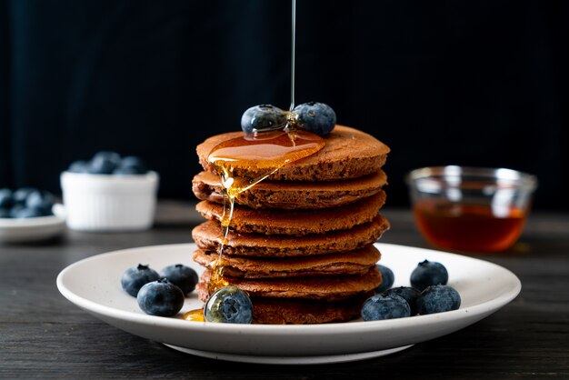 Chocolate pancake stack with blueberryies and honey on plate