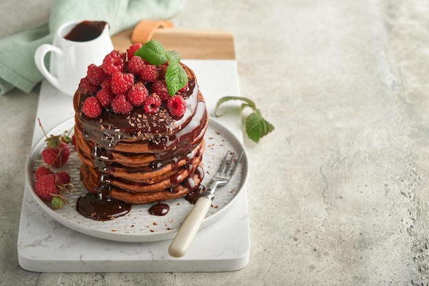 Chocolate Pancakes Pancakes with fresh raspberry with chocolate glaze or toppings in gray bowl on light gray table background Homemade classic american pancakes Page for magazine concept