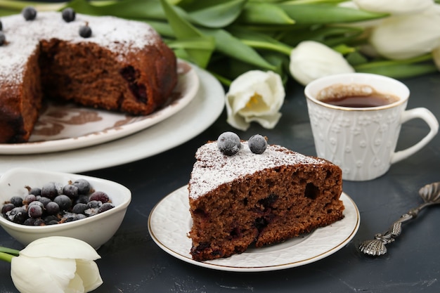 Chocolate pie with black currant on a dark, on the table there is a cup of coffee and white tulips