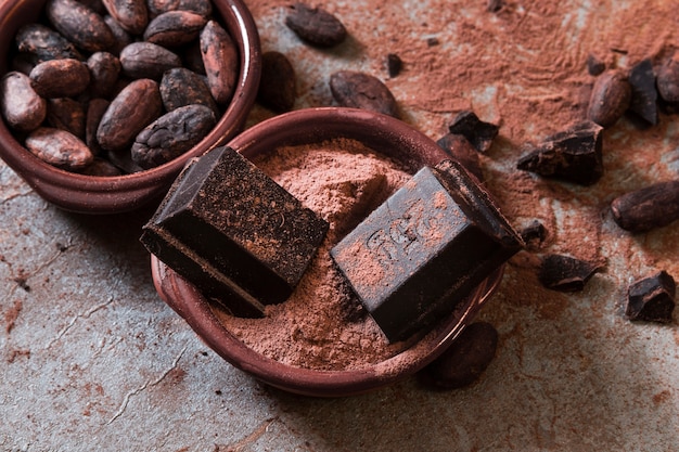 Foto pezzi di cioccolato su polvere di cacao e fagioli sopra il tavolo