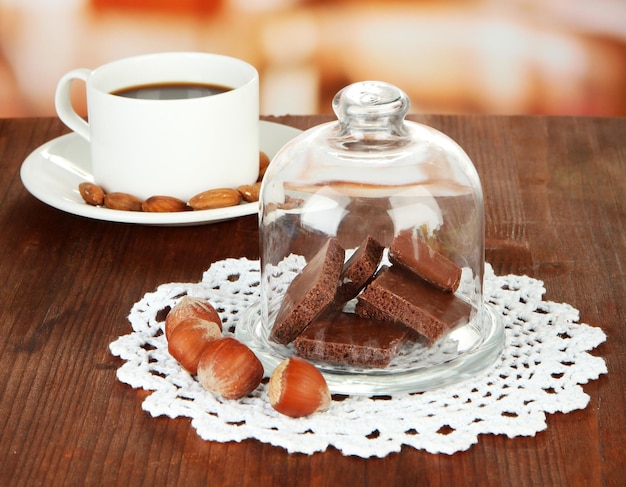 Chocolate pieces under glass cover and hot drink on bright background