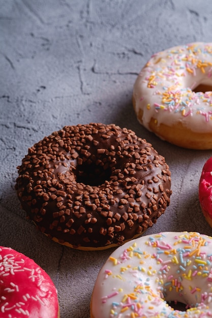 Chocolate, pink and vanilla donuts with sprinkles, sweet glazed dessert food on concrete textured background, angle view macro