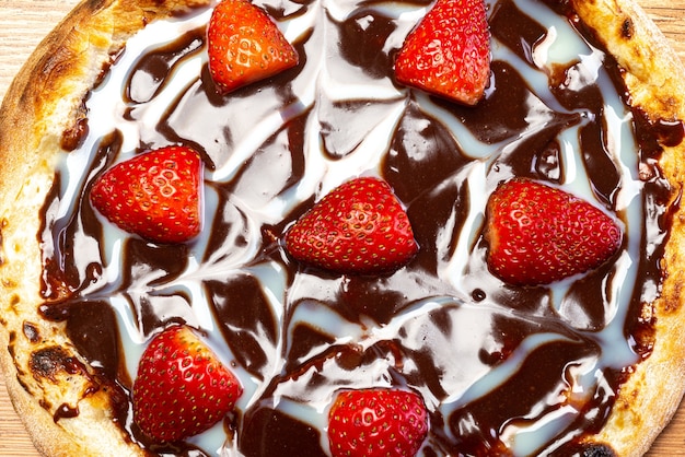 chocolate pizza with strawberry and sour cream sauce served on a wooden table top view close up