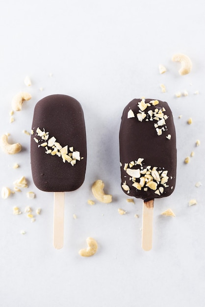 Chocolate popsicle ice cream on a stick with cashews on a light background