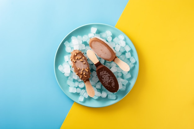 Chocolate popsicles and crushed ice on blue plate on yellow and blue table