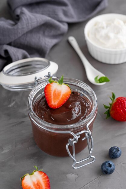 Chocolate pudding with fresh berries and whipped cream in a glass jar on a gray concrete background