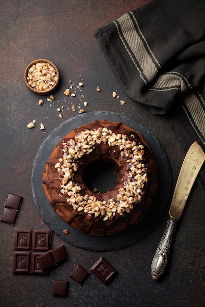 Chocolate and pumpkin bundt cake with chocolate glaze and walnut on dark concrete background.