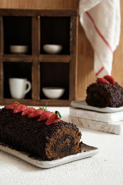 Photo chocolate roll cake on white background strawberry slices on top as garnish bolu gulung coklat