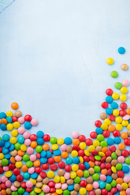 Chocolate round candy in a multicolored sugar glaze on light blue table. Selective focus. Top view. Place for text.