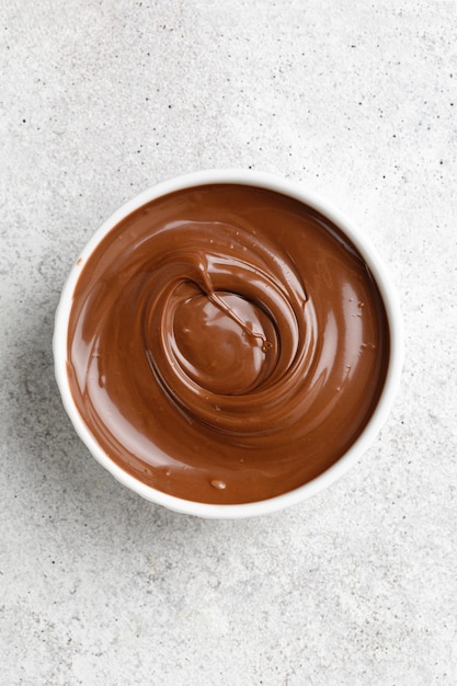 Chocolate sauce in a white saucer on grey background Curl of Liquid chocolate Top view