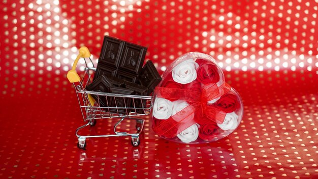 Chocolate in shopping trolley and roses gift on red background. 14 february sale. Creative minimal concept